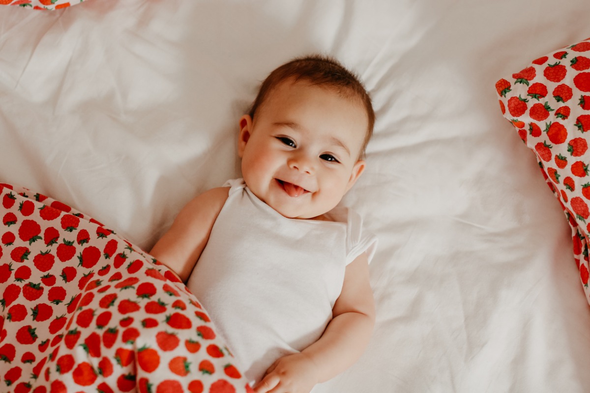 Bebê sorridente deitada e coberta com cobertor com estampa de morangos